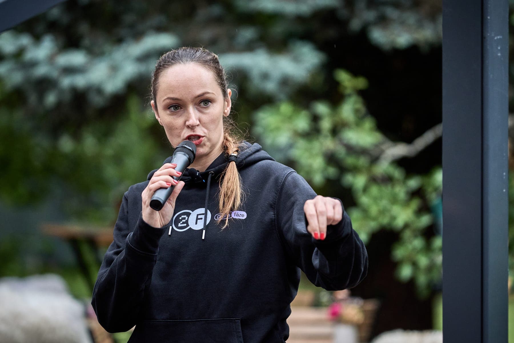Kája mluví do mikrofonu a gestikuluje
